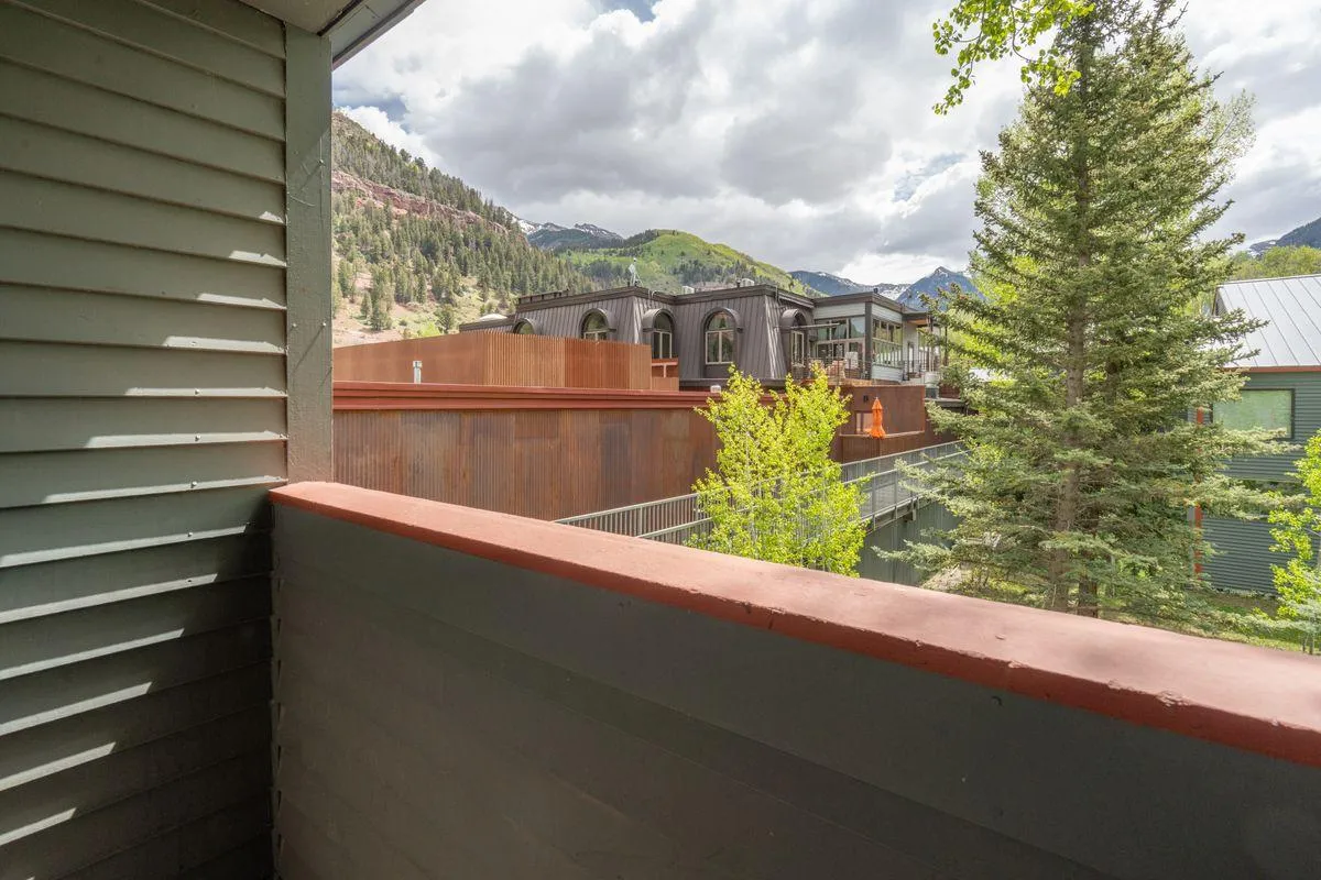 A tranquil balcony scene offers panoramic views of distant mountains and lush green trees, with hints of modern architectural elements. The space invites relaxation—ideal for sipping morning coffee, soaking in the fresh mountain air, or observing seasonal changes in the landscape.