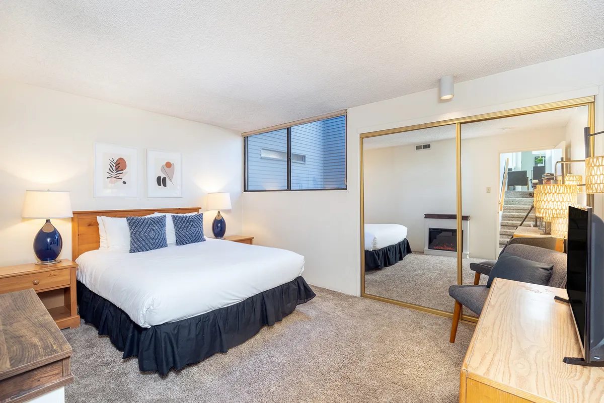 A comfortable queen bedroom complete with mirrored closet, nightstands, and a television. The large window fills the room with natural light, creating a welcoming space for adults or grandparents seeking privacy and relaxation.