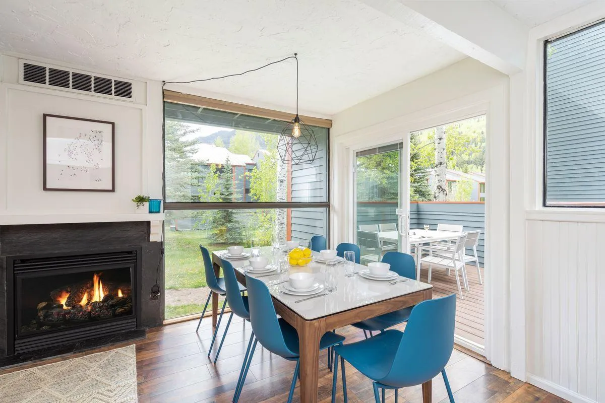 The image showcases a beautifully updated dining area set for a meal, a glowing fireplace creating a cozy ambiance, and expansive windows that flood the space with natural Telluride light. The scene evokes comfort and connection, perfect for family gatherings and memorable evenings indoors.