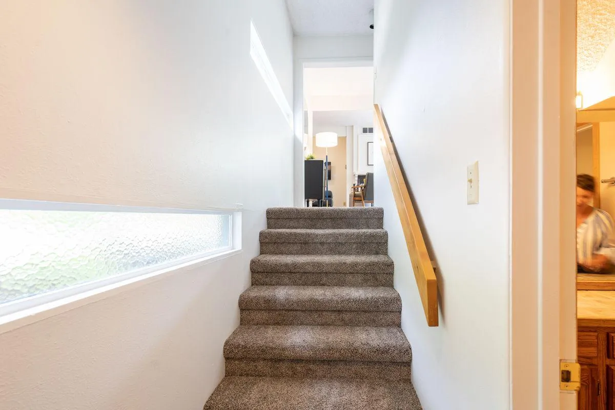 A staircase receives generous daylight from a nearby window, complemented by the textured carpet and a welcoming landing. This transitional space subtly conveys the 'homecoming' feeling and the organized entryway experience, echoing the section's promise of a warm welcome and easy flow between outdoor and indoor living.