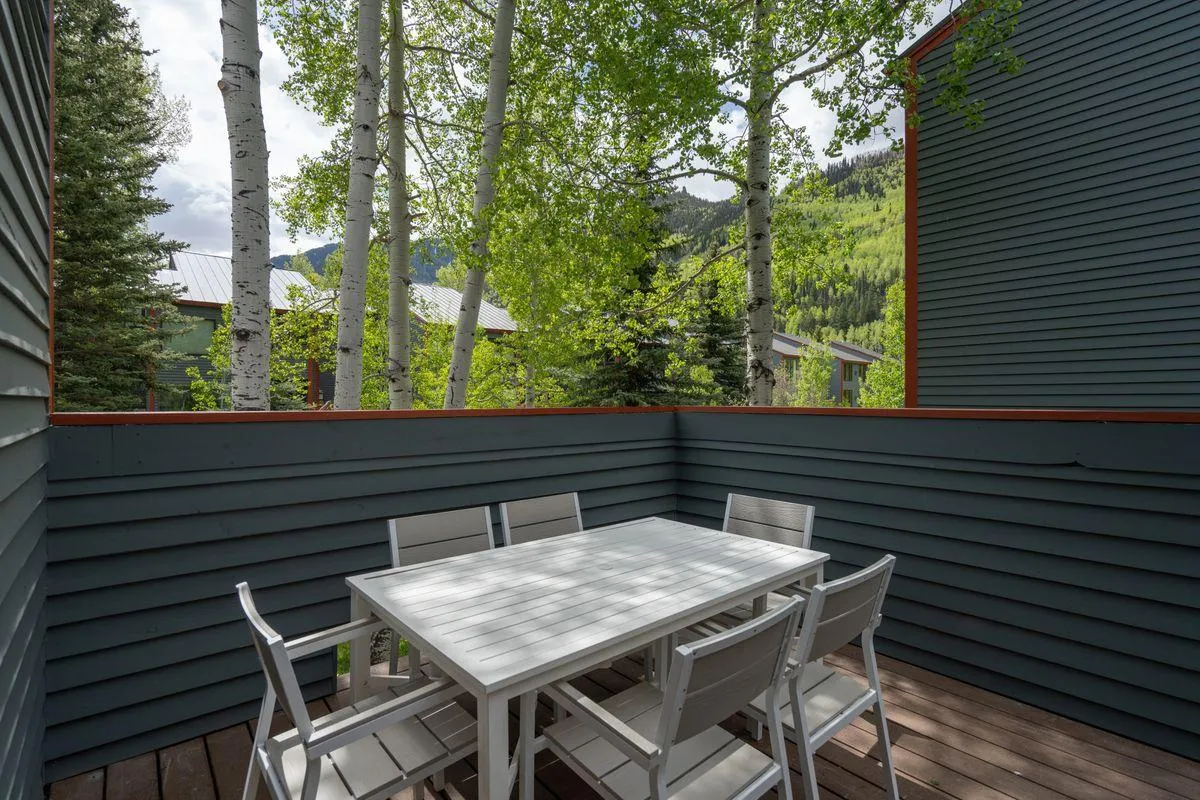 A serene private deck with an outdoor dining table surrounded by trees and offering a picturesque mountain view. The space is designed for al fresco dining, morning coffee, or relaxing in the fresh Colorado air.