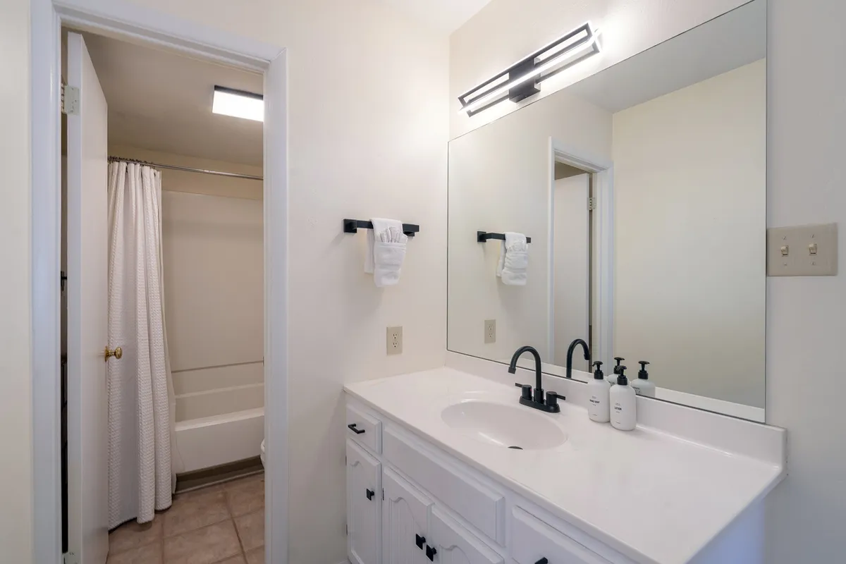 A modern en suite bathroom with a large mirror, vanity with sink, and a spacious shower area. The space is bright and fresh, perfect for unwinding after an active day or for tranquil morning routines.