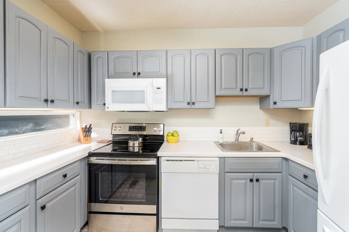 A bright, fully equipped kitchen with modern gray cabinetry, stainless steel appliances, white countertops, and a kitchen sink. The space is practical and inviting, ideal for both everyday meals and special culinary moments.